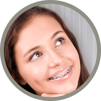 A young woman smiles while looking up with braces in front of a gray backdrop.