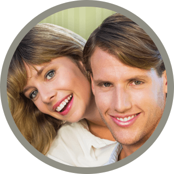 A couple, man and woman, smiles together in front of a green backdrop.